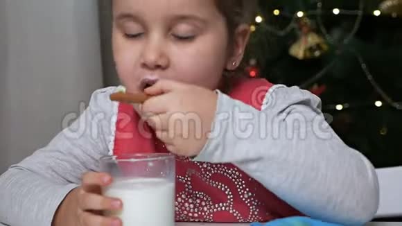 可爱的孩子在圣诞树附近吃姜饼喝一杯牛奶视频的预览图