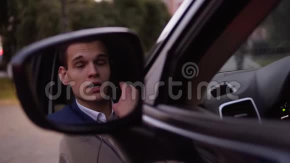 英俊严肃的商人西装革履穿着白色衬衫在车里用手机说话汽车车门上的反光视频的预览图