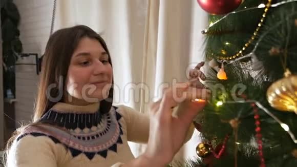 穿着圣诞毛衣微笑着装饰圣诞树挂玩具的年轻幸福女子视频的预览图