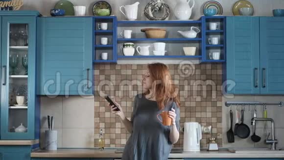 女人红发打开智能手机音乐在厨房里劲舞视频的预览图