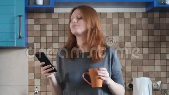 红发美女打开智能手机音乐在厨房跳舞视频的预览图