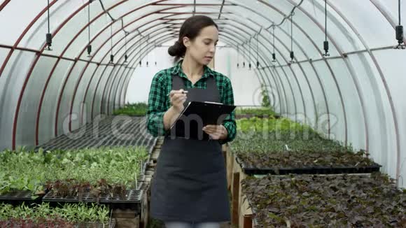 白种人的女农民正在计算幼苗并在站在温室里的剪贴板上写字农业概念视频的预览图