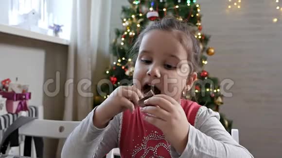 圣诞前夜坐在圣诞树旁吃巧克力圣诞老人的女孩在家庆祝圣诞节视频的预览图
