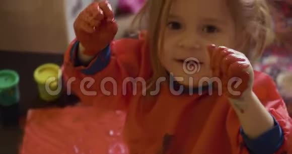 快乐的小女孩用手画红色的颜料视频的预览图