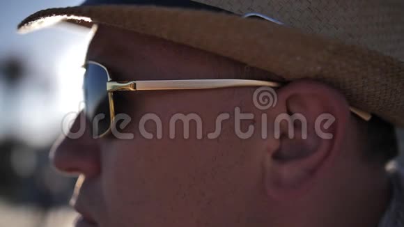 一个戴着墨镜和帽子的人正坐在海滩上经过人们看着大海视频的预览图