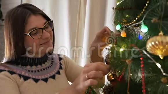 穿着圣诞毛衣微笑着装饰圣诞树挂玩具的年轻幸福女子视频的预览图