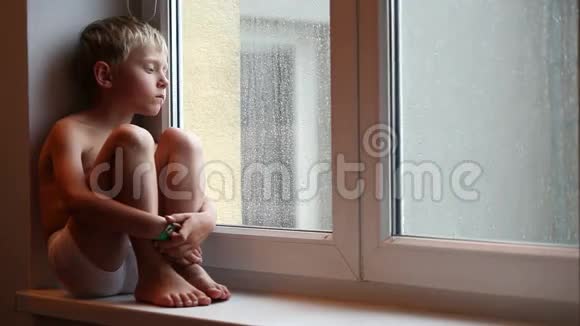 孤独的小男孩等着他的父母坐在窗台上回家视频的预览图