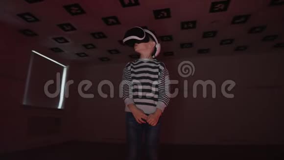 小男孩在虚拟现实中环顾四周戴着耳机房间里闪烁着红色和蓝色的霓虹灯视频的预览图
