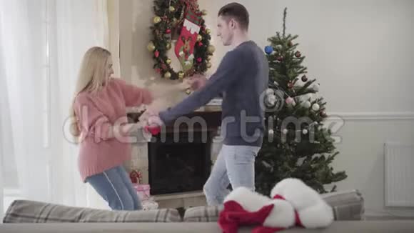 年轻的高加索男人和女人在家里的圣诞树前跳舞积极的一对夫妇在除夕度过视频的预览图
