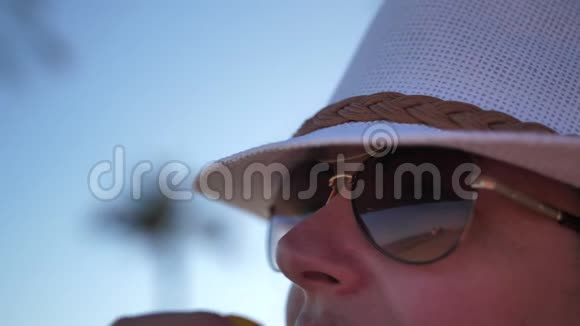 带着太阳镜和帽子的旅行妇女看着大海和路过的人视频的预览图