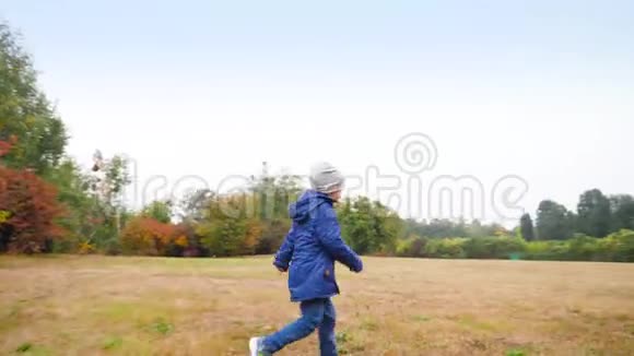 秋天欢快的小男孩在森林旁边的草地或田野上快速奔跑视频的预览图