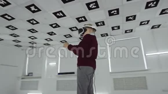 穿着棕色毛衣的小男孩正在虚拟现实中玩射击游戏他在空荡荡的游戏室里戴着耳机视频的预览图