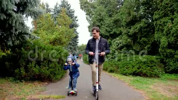 快乐的年轻父亲和小儿子在秋天公园骑滑板车的视频一家人玩得开心视频的预览图
