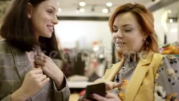 女人在商场的服装店里聊天看着对方的树枝和智能手机屏幕视频的预览图