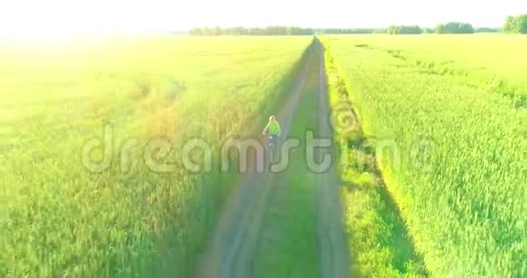 鸟瞰年轻男孩骑着自行车穿过古老的乡村道路上的麦田阳光和光束视频的预览图