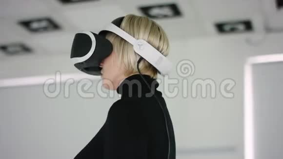 一个年轻女子的特写镜头她戴着虚拟现实耳机站在一个充满白色照明的游戏室里跟踪视频的预览图