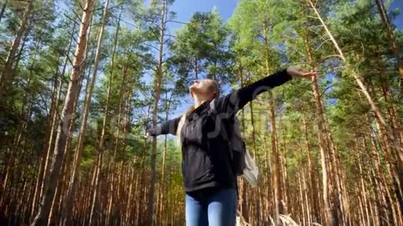 美丽的微笑女子在森林里徒步旅行双手伸向太阳树木和蓝天视频的预览图