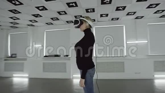 年轻女子正把虚拟现实耳机放在头上并在一个充满白色霓虹灯的空玩室里取下视频的预览图