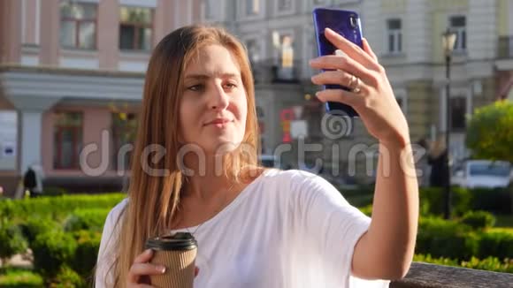 一幅美丽的年轻女子留着长发在智能手机相机上自拍咖啡可以放进纸杯视频的预览图