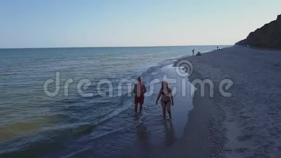 男人和女人在日落时沿着海滩散步追踪一对夫妇在度假时在海滩上玩得开心的航拍照片视频的预览图