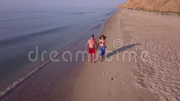 男人和女人在日落时沿着海滩散步追踪一对夫妇在海滩上玩得开心的空中镜头视频的预览图