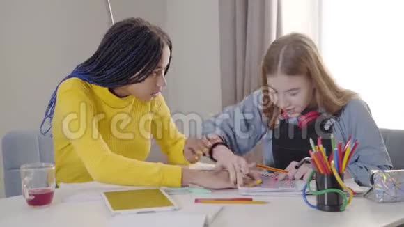 非裔美国女孩把笔记本放在白种人朋友桌子上愤怒的青少年折断铅笔两名学生视频的预览图
