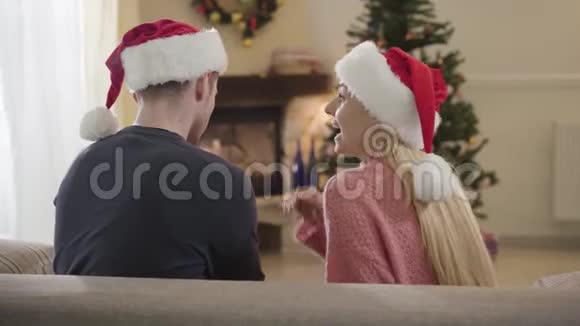 兴奋的白种人女人戴着红色的圣诞帽在丈夫耳边低语拍手年轻夫妇视频的预览图