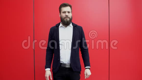 自信的胡子男正站在红墙附近的摄像机前交叉着双手看着手表关闭视频的预览图