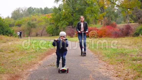 4k视频4岁的微笑男孩骑着滑板车和他的母亲在秋天公园视频的预览图