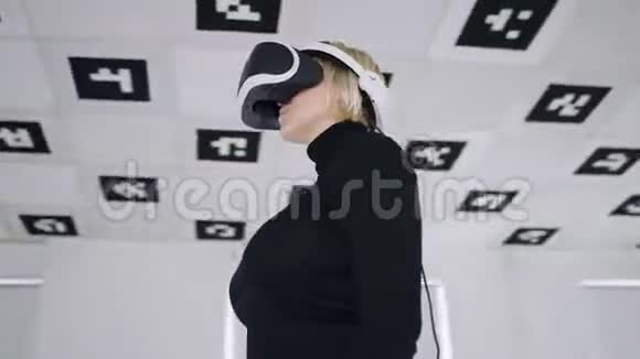 成年女性在一个白色照明的大空游戏室里用虚拟现实耳机环顾四周追踪弧线视频的预览图