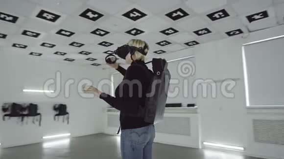 虚拟现实耳机中的成年女性在一个充满白光的大空游戏室中使用控制器跟踪弧线视频的预览图