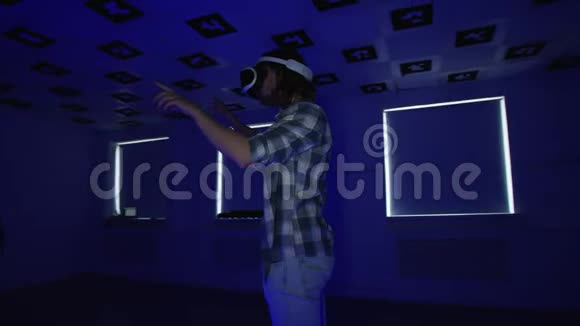 一个穿着vr耳机的年轻人在一个充满闪烁的红色和蓝色霓虹灯的空玩室里做手势跟踪视频的预览图