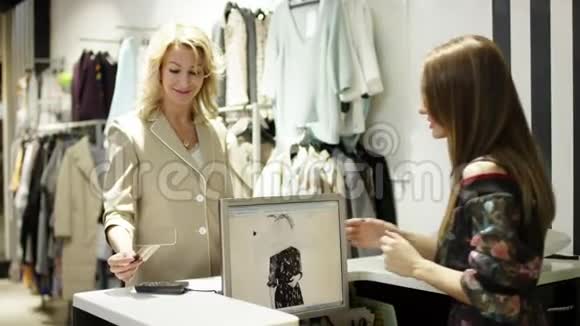 漂亮的中年金发女人用信用卡在商场的服装店买衣服视频的预览图