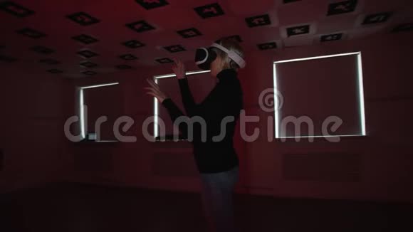 虚拟现实耳机里的年轻女子站在一个充满红色眨眼的空玩室里做手势视频的预览图