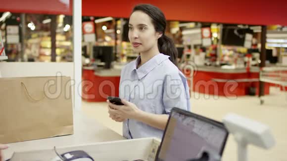 迷人的年轻女性用智能手机进行无线支付用NFC技术在收银台进行非接触式支付视频的预览图