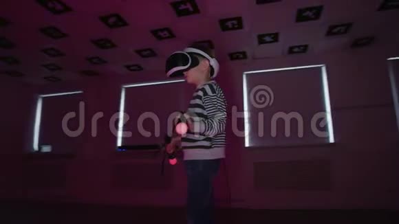 漂亮的小男孩正在虚拟现实中玩电子游戏戴着耳机在房间里闪烁着霓虹灯视频的预览图
