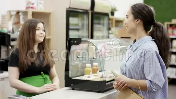 美丽的女人拿着一捆钞票向美丽的年轻微笑咖啡师要咖啡和甜点并用现金支付视频的预览图