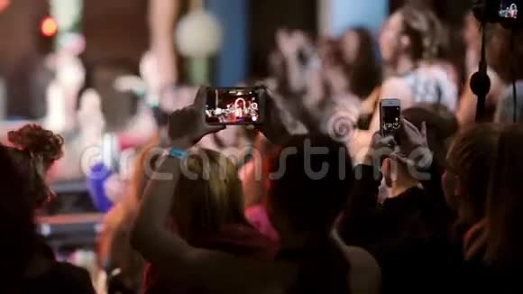 一些女孩在智能手机上拍摄的特写镜头背景上模糊快乐欢呼的人群视频的预览图