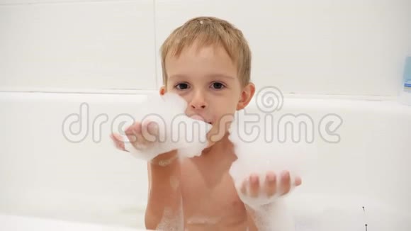 4k特写视频快乐的小男孩坐在浴缸里玩肥皂泡沫和泡泡视频的预览图