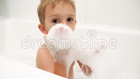 4k视频快乐微笑的小男孩正在洗澡并在镜头中吹肥皂沫视频的预览图