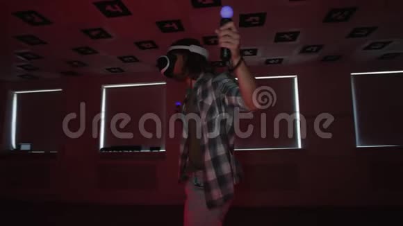 一个穿着vr耳机的年轻人在一个充满红色和蓝色闪烁的空玩室里用控制器做游戏视频的预览图