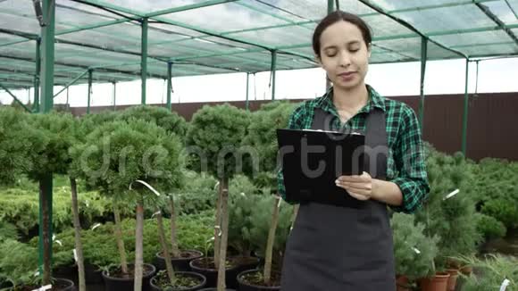 站在温室里用剪贴板做笔记的年轻女人女农民视频的预览图