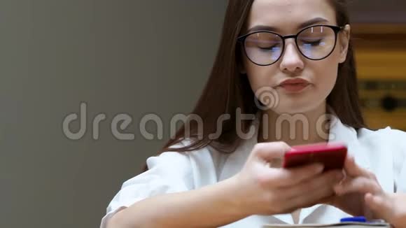 带眼镜的年轻女孩使用智能手机近距离学生手里拿着红色的电话视频的预览图