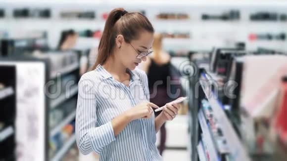 化妆品店戴眼镜的女孩用手机看手机屏幕动作慢视频的预览图
