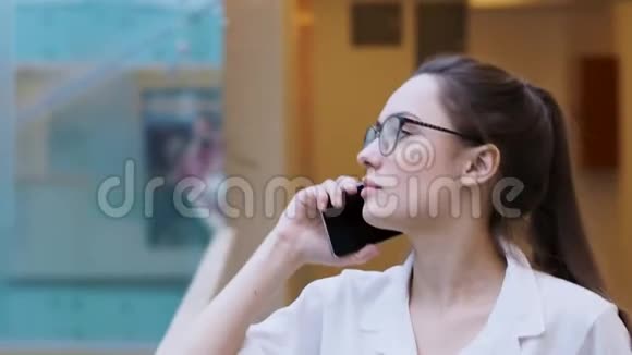 年轻的商务女士使用智能手机穿着白色衬衫和眼镜的惊讶女孩打了个电话视频的预览图