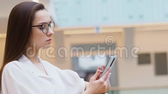 年轻女性穿着时尚的商务服装和眼镜使用智能手机与聊天机器人交流视频的预览图