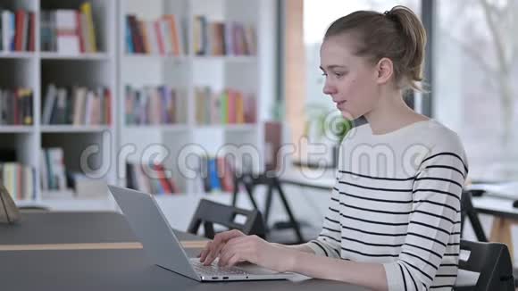 在图书馆里用笔记本电脑庆祝成功的年轻女子视频的预览图