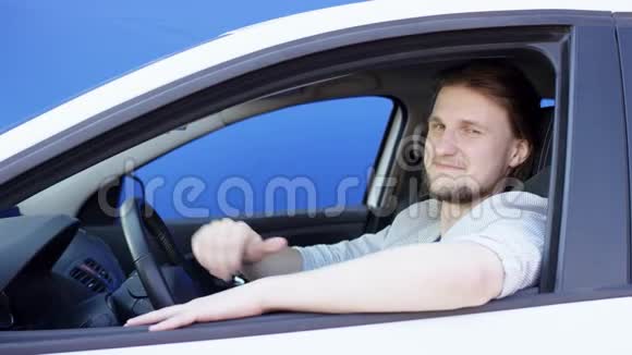坐在车里的人伸出大拇指对着镜头微笑坐在他车里的年轻人的左视图视频的预览图