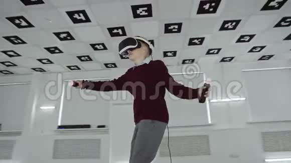 穿着棕色毛衣的小男孩正在虚拟现实耳机中跳舞在一个空的游戏室里使用控制器视频的预览图