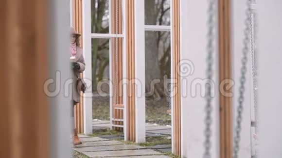 穿着棕色外套的年轻女子拿着一杯咖啡走在秋千边视频的预览图